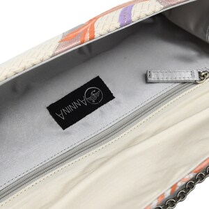 Puede incluir: El interior de un bolso de mano blanco con un bolsillo con cremallera y una correa de cadena plateada. El bolso tiene una etiqueta negra con la palabra "ANNINA" y un logotipo de p&aacute;jaro.