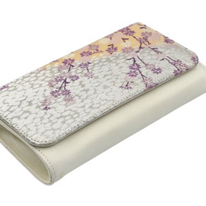 May include: A white leather wallet with a floral pattern on the front flap. The pattern features purple and yellow flowers on a silver background.