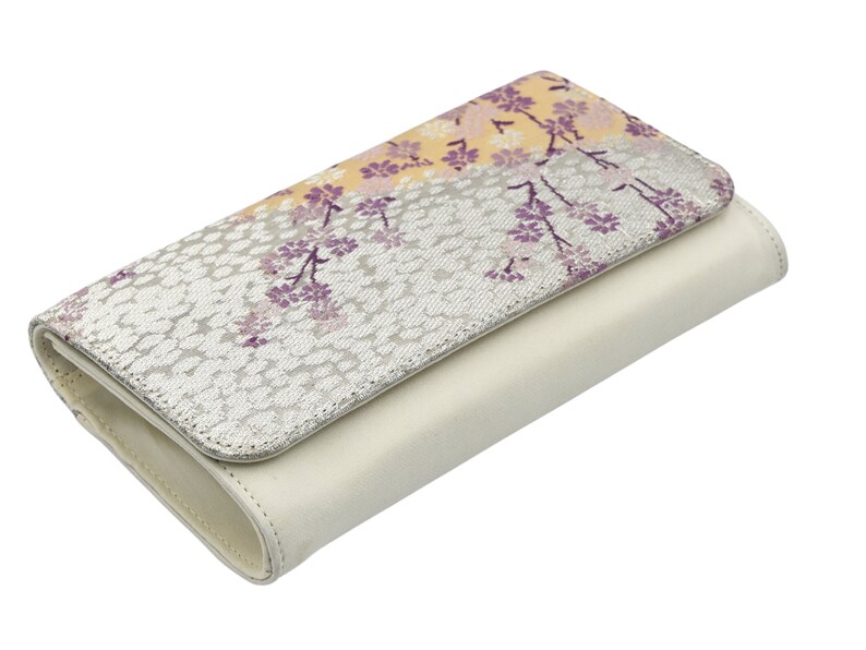 May include: A white leather wallet with a floral pattern on the front flap. The pattern features purple and yellow flowers on a silver background.