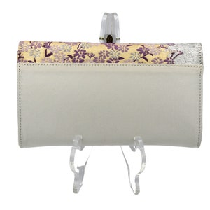 May include: A white leather wallet with a floral pattern on the front flap. The wallet is on a clear plastic stand.