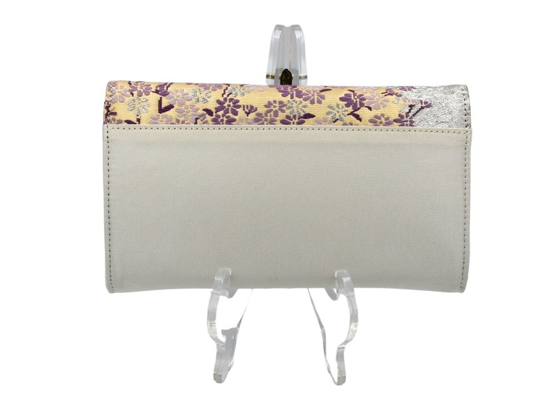 May include: A white leather wallet with a floral pattern on the front flap. The wallet is on a clear plastic stand.
