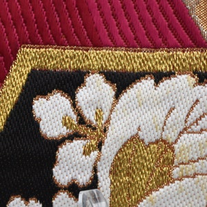 K&ouml;nnte beinhalten: Nahaufnahme eines schwarzen Stoffes mit goldenen und wei&szlig;en Stickereien. Die Stickerei zeigt ein florales Design mit wei&szlig;en Bl&uuml;tenbl&auml;ttern und goldenen Akzenten.