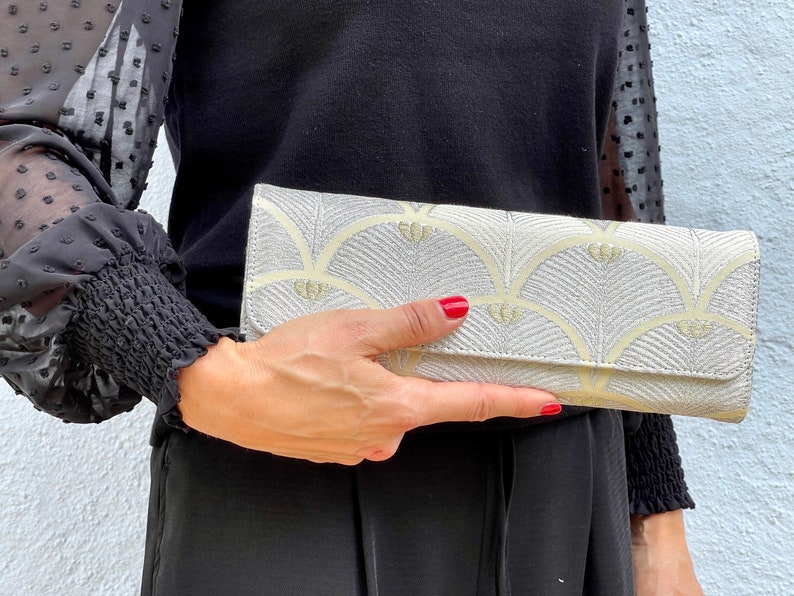 May include: A silver clutch bag with a yellow and white geometric pattern. The clutch has a flap closure and a silver zip.