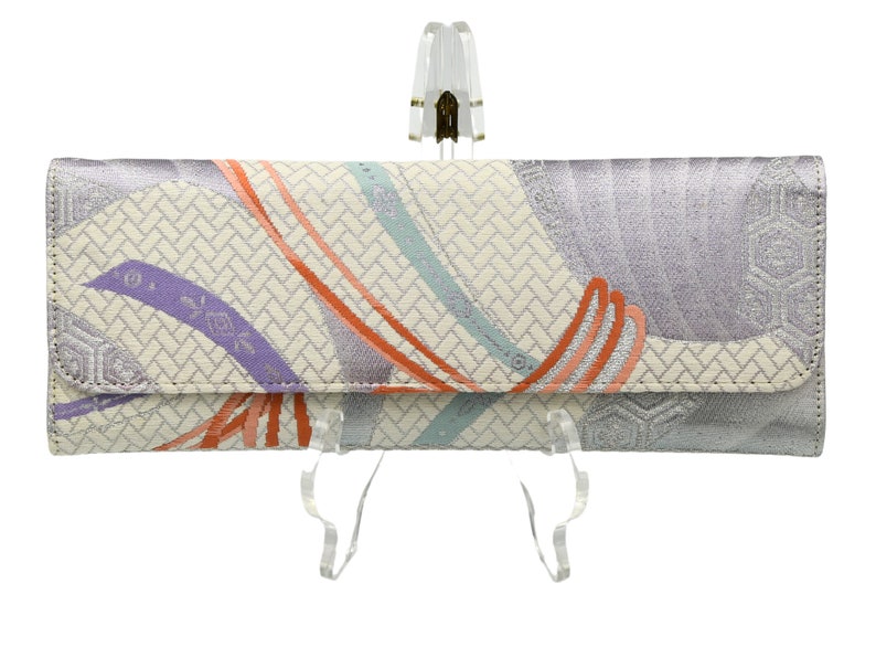 Puede incluir: Un bolso de mano blanco y plateado con un estampado floral colorido. El bolso tiene un cierre de solapa y una cremallera plateada.