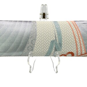 Puede incluir: Un bolso de mano plateado con un dise&ntilde;o estampado en blanco y azul. El patr&oacute;n presenta un dise&ntilde;o geom&eacute;trico con una textura tejida y un motivo floral azul y naranja.