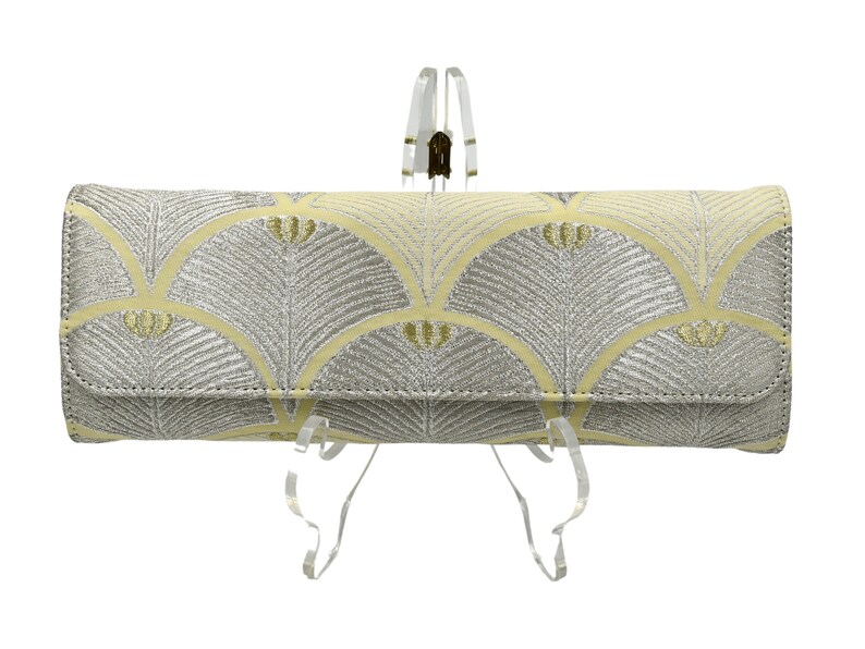May include: A yellow and silver clutch bag with a geometric pattern. The bag is on a clear stand.