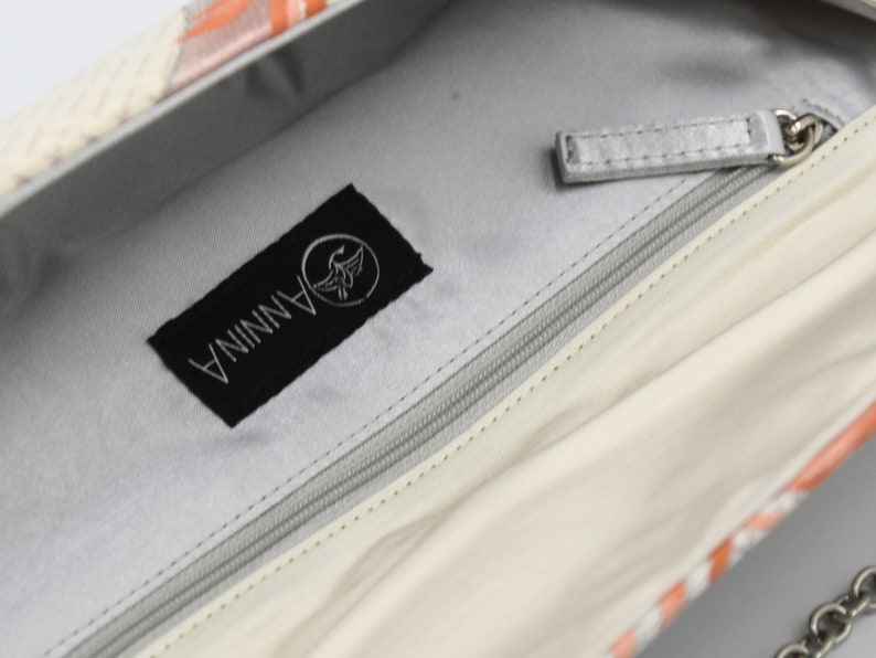 Puede incluir: El interior de un bolso blanco con una etiqueta negra que dice "ANNINA" con un logotipo de p&aacute;jaro. El bolso tiene una cremallera y un tirador de cremallera plateado.