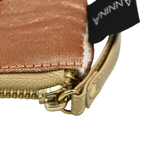 K&ouml;nnte beinhalten: Nahaufnahme eines goldenen Rei&szlig;verschlusses an einer beigefarbenen Stofftasche mit einem rosa-goldenen gestreiften Stofffutter. Die Tasche hat einen braunen Lederriemen mit einem Metallverschluss und ein schwarzes Etikett mit dem aufgedruckten Wort "ANNINA".