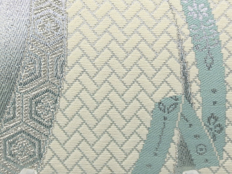 Puede incluir: Primer plano de una tela con fondo blanco y un patr&oacute;n plateado y azul claro. El patr&oacute;n es una combinaci&oacute;n de formas geom&eacute;tricas y dise&ntilde;os florales.