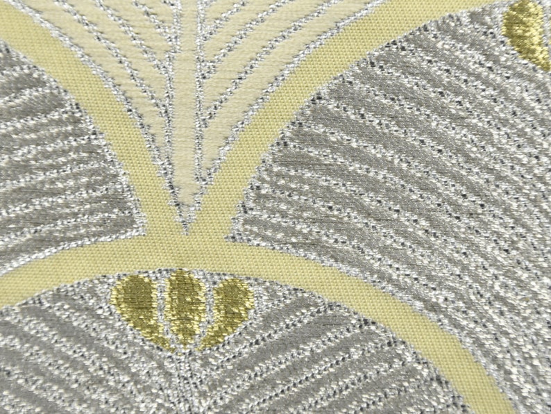May include: Close-up of a fabric with a silver and yellow geometric pattern. The pattern features overlapping fan shapes with a textured, woven look.