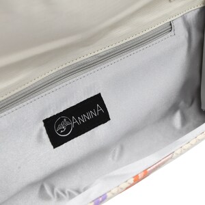 Puede incluir: El interior de un bolso de mano de color gris claro con una etiqueta de tela negra que dice "ANNINA" en letras blancas.
