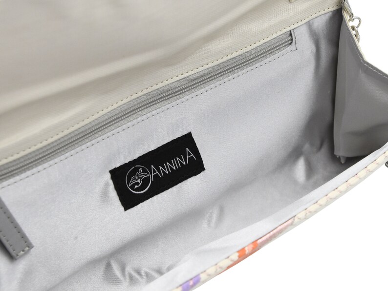 Puede incluir: El interior de un bolso de mano de color gris claro con una etiqueta de tela negra que dice "ANNINA" en letras blancas.