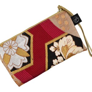 K&ouml;nnte beinhalten: Eine rote, schwarze und goldene Clutch mit floralem Muster und einem goldenen Rei&szlig;verschluss. Die Clutch hat einen langen Riemen.