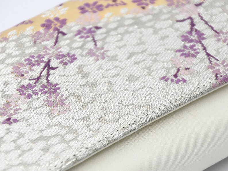May include: A white clutch purse with a silver floral pattern and a white lining. The floral pattern features purple and pink flowers.