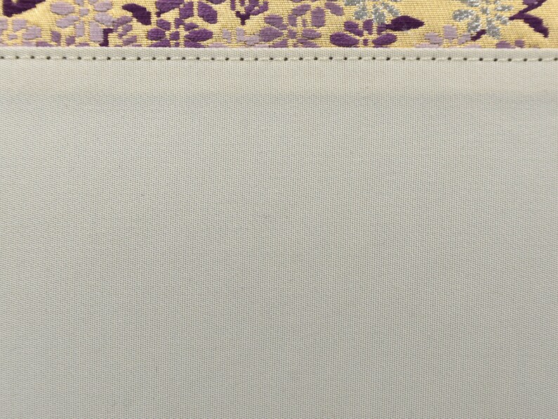 May include: A close-up of a light gray fabric with a subtle texture. The fabric has a stitched seam along the top edge.
