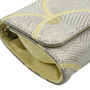 May include: A small, pale yellow clutch bag with a silver and gold patterned design. The bag has a flap closure and a silver zipper.