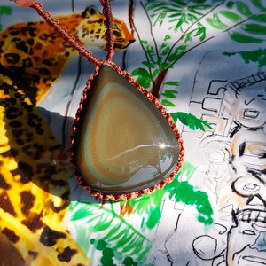 Könnte beinhalten: Eine braune Lederkordelkette mit einem tropfenförmigen, irisierenden Obsidian-Anhänger. Der Anhänger hat eine dunkelgrüne und braune Farbe mit einem schimmernden Effekt.