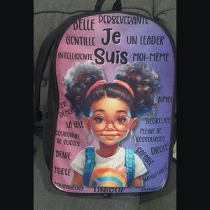 Peut inclure: Un sac à dos rose et violet avec un motif arc-en-ciel coloré et une illustration de dessin animé d'une jeune fille portant des lunettes. Le sac à dos porte le texte "Je Suis" en grandes lettres et d'autres mots français autour de l'image.
