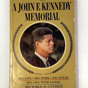 May include: A gold-colored book cover with a black and white photo of John F. Kennedy. The title is "A John F. Kennedy Memorial" and the text below the photo reads "His Life, His Work, His Deeds, His Life With Jackie, His World As A Father, His Last Day On Earth".