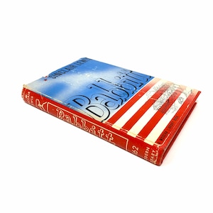 May include: A red and blue hardcover book titled "Babbitt" by Sinclair Lewis. The book cover features a red, white, and blue striped design with a small illustration of a city.