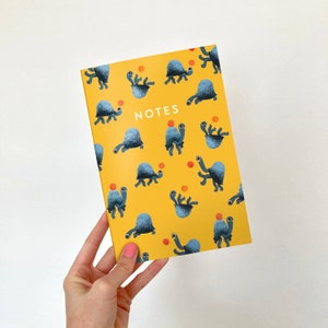 May include: A yellow notebook with a pattern of blue turtles carrying orange balls. The notebook says "NOTES" in white text.