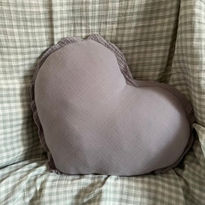 May include: A heart-shaped pillow with a soft, gray fabric and a ruffled edge. The pillow is sitting on a green and white checkered fabric.