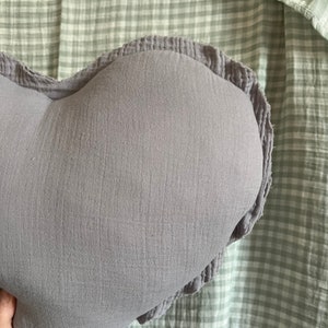 May include: A soft, heart-shaped pillow with a ruffled edge. The pillow is made of a light purple fabric.