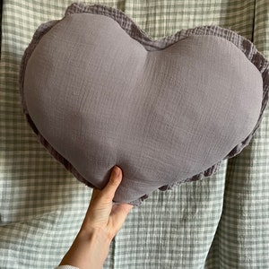 May include: A heart-shaped pillow with a ruffled edge, made of a soft, light purple fabric.