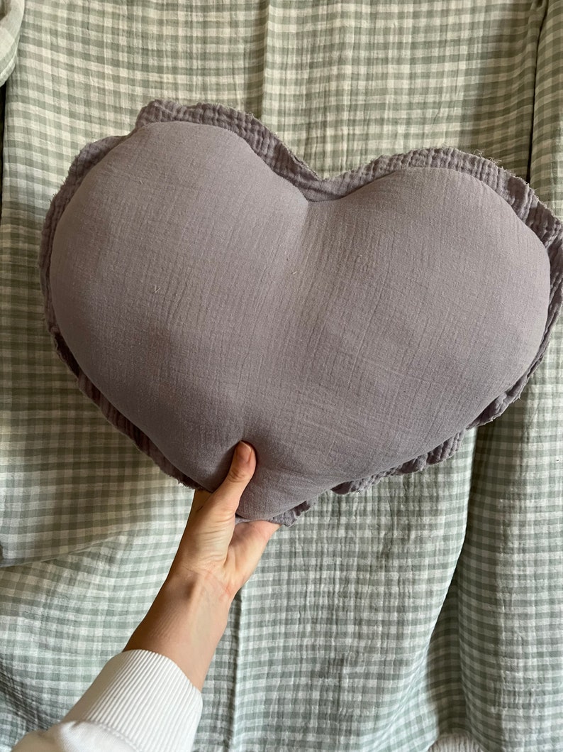 May include: A heart-shaped pillow with a ruffled edge, made of a soft, light purple fabric.