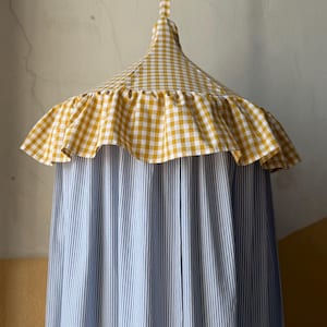 Puede incluir: Un dosel colgante con una parte superior de cuadros amarillos y blancos y un borde con volantes. El cuerpo del dosel es de tela a rayas azules y blancas. Se suspende de una correa de tela a cuadros a juego.