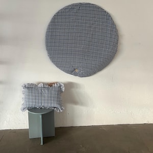 May include: A round, blue and white gingham patterned play mat with a small pillow in the same pattern. The pillow has a white fringe around the edges.