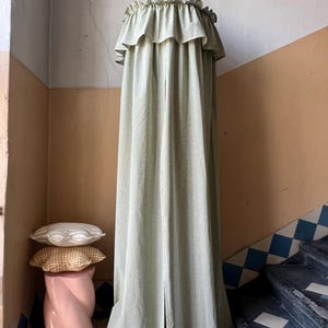 May include: A green and white gingham canopy with a ruffled top hangs from the ceiling in a room with a pink pedestal and patterned pillows.