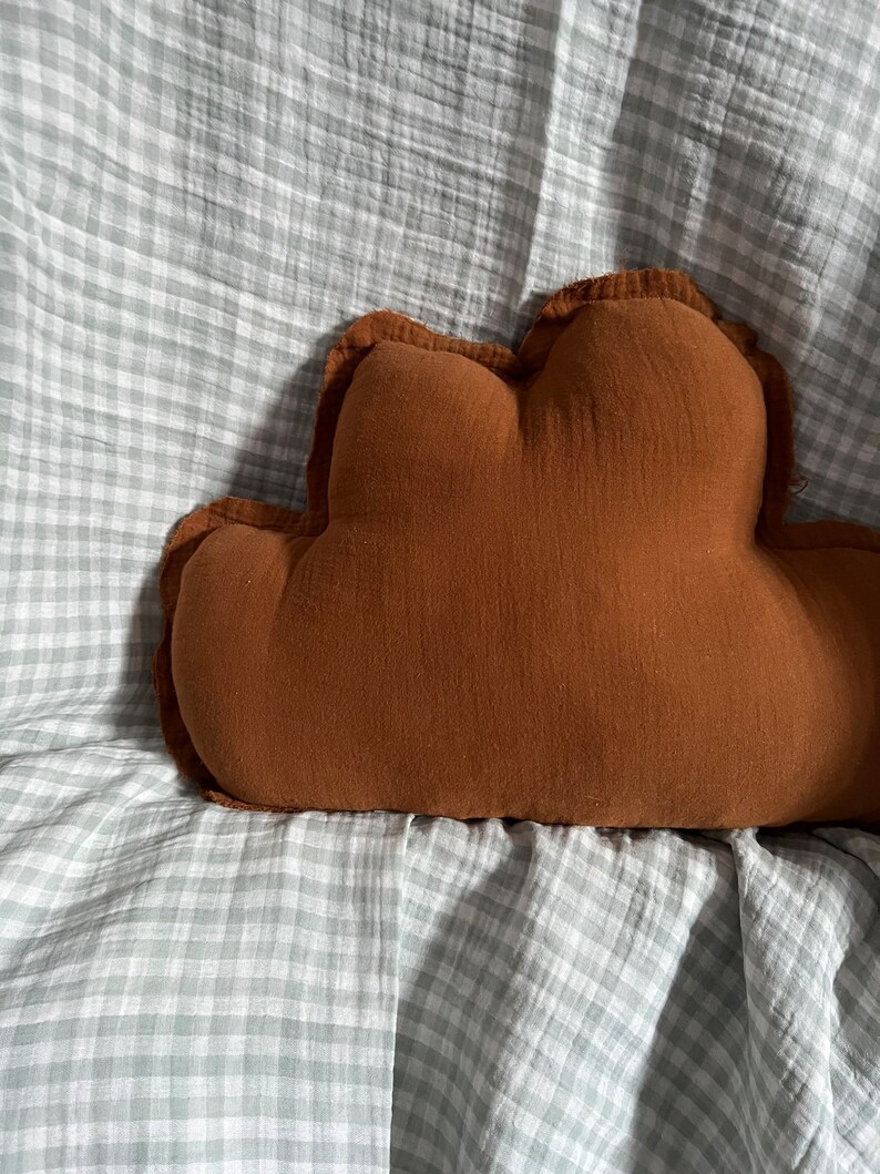 May include: A brown cloud-shaped pillow on a gray and white gingham fabric.