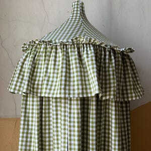 Può includere: Un baldacchino a quadretti verdi e bianchi con un bordo a balze. Il baldacchino è sospeso da un punto centrale e ha una forma svasata, a campana. Il tessuto presenta un classico motivo a quadretti.