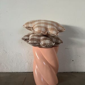 May include: Two brown and white gingham patterned cushions stacked on top of each other on a pink twisted pedestal stool.