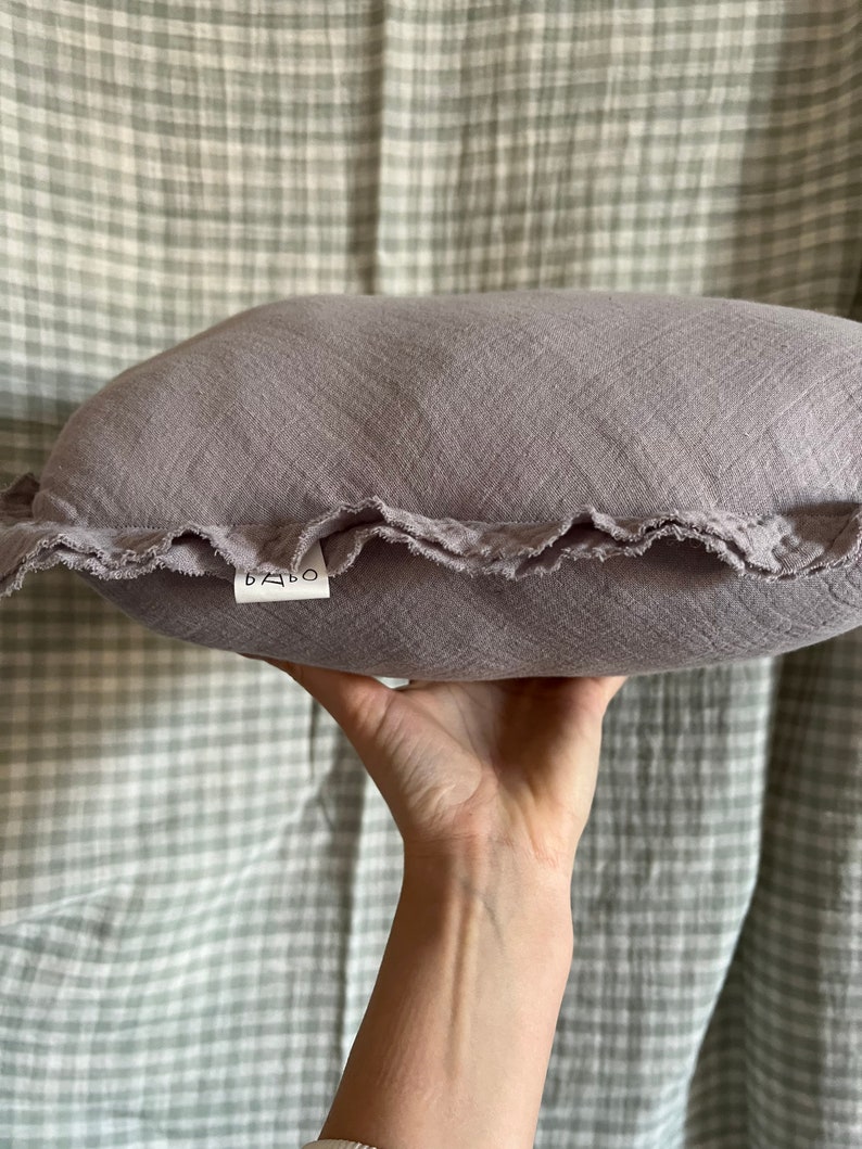 May include: A soft, gray, ruffled pillow with a white label that says "BABO" on it.