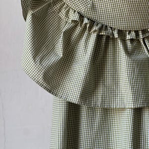 May include: A green and white gingham dress with a ruffled neckline. The dress has a tiered skirt.