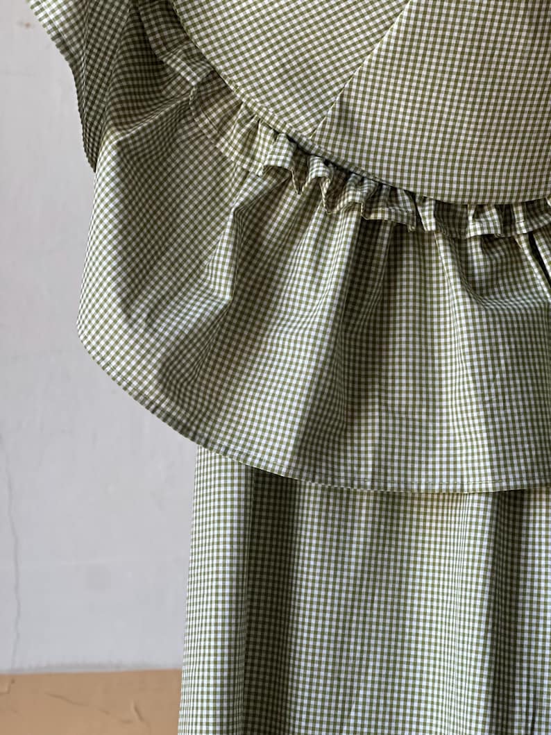 May include: A green and white gingham dress with a ruffled neckline. The dress has a tiered skirt.