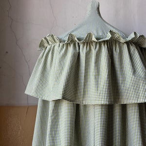 May include: A green and white gingham canopy with a ruffled edge. The canopy is suspended from a white ceiling.