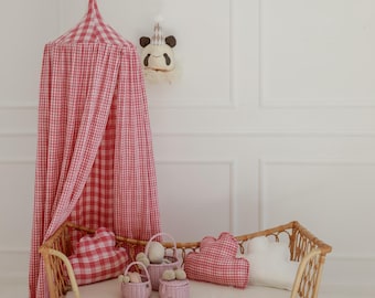 Puede incluir: Una escena de habitación infantil con una cama de ratán, un dosel a cuadros rojos y blancos y accesorios a juego. Incluye cojines decorativos, cestas y un adorno de pared de panda. Ambiente suave y neutro.