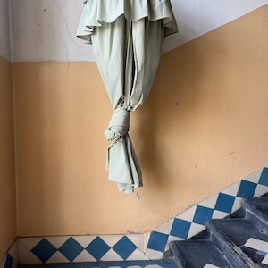 May include: A green and white checkered fabric canopy hangs from the ceiling of a room with a tiled floor. The canopy is gathered at the bottom and tied in a knot.