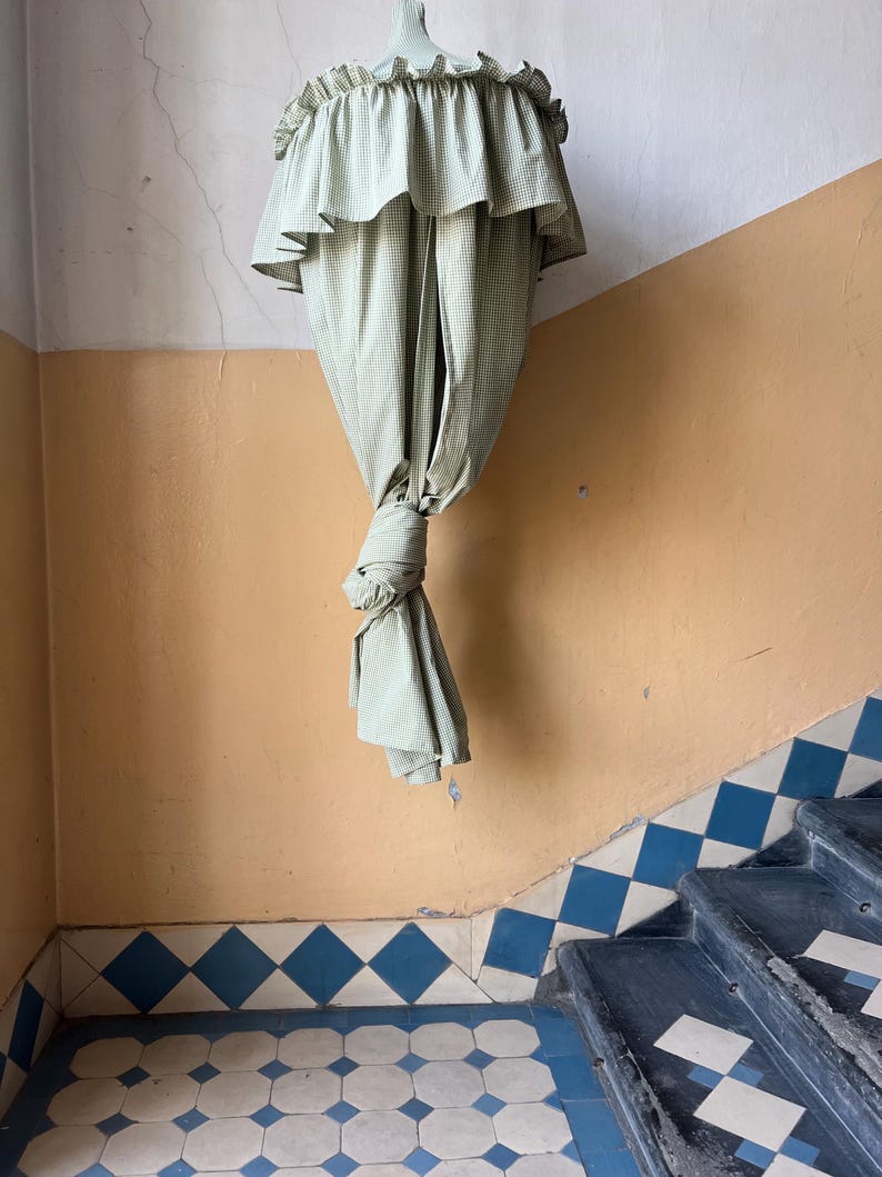 May include: A green and white checkered fabric canopy hangs from the ceiling of a room with a tiled floor. The canopy is gathered at the bottom and tied in a knot.