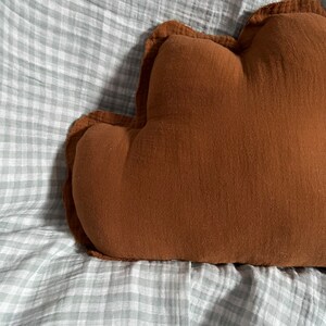 May include: A brown cloud-shaped pillow with a ruffled edge, resting on a white and gray gingham fabric.