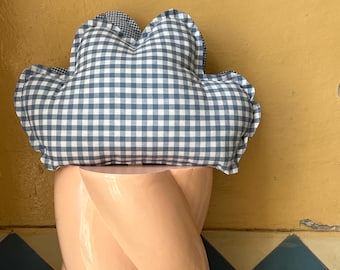 Könnte beinhalten: Ein wolkenförmiges Kissen mit blau-weißem Vichy-Muster liegt auf einem pfirsichfarbenen, gedrehten Sockel. Das Kissen hat einen gerüschten Rand und ein kontrastierendes Vichy-Muster auf der Unterseite. Der Sockel hat eine glänzende Oberfläche.