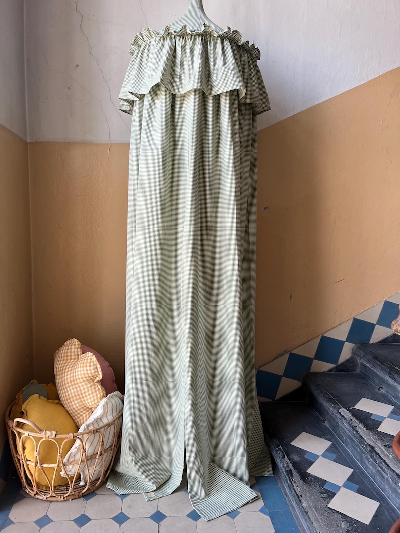 May include: A green and white gingham canopy with a ruffled top. The canopy is hanging from a ceiling hook and is draped over a set of stairs.