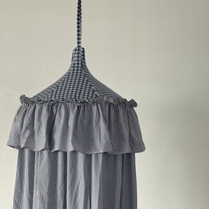 May include: A blue and white striped canopy with a gingham top and ruffled trim. The canopy is hanging from a white ceiling.