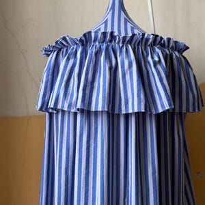 May include: A blue and white striped off-the-shoulder top with a ruffled neckline. The fabric is vertically striped, and the top is hanging on a matching striped hanger.