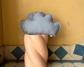 Könnte beinhalten: Ein rosa, gedrehter Sockeltisch trägt ein wolkenförmiges Kissen. Das Kissen ist blau-weiß kariert. Der Hintergrund ist eine gelbe Wand und ein gemusterter Fliesenboden.