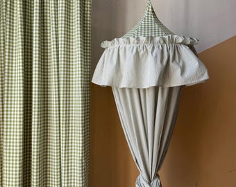 May include: A green and white gingham patterned curtain and a matching canopy with a ruffled edge. The canopy is suspended from the ceiling and has a striped fabric that is knotted at the bottom. The color scheme is a soft green and white.