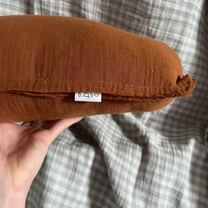 May include: A brown, rectangular pillow with a white label that says "BABO" on it.